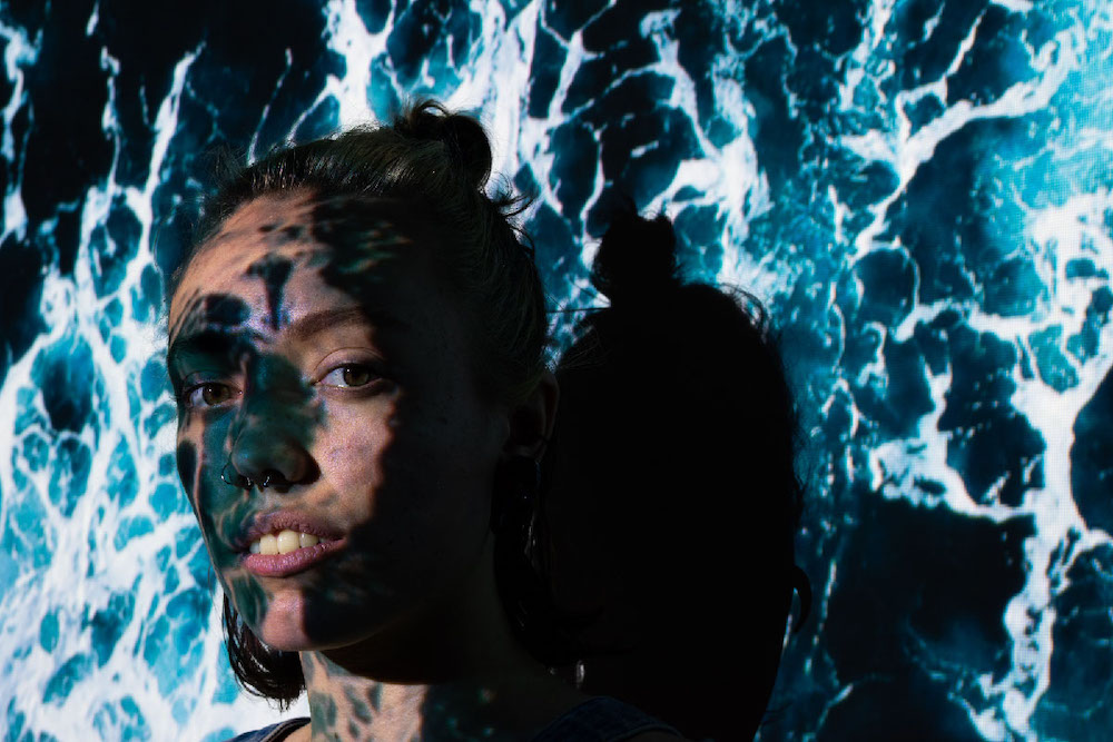 Girl standing looking directly into the camera with a blue ocean projected on her face.